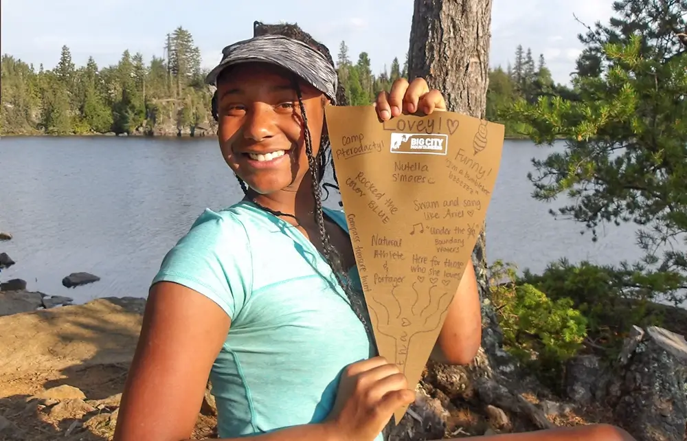 Lovey facing the camera while holding a Big City Mountaineers flag covered with handwritten signatures.
